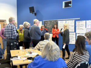En grupp personer deltar i en workshop i samlingssalen i Fröseke Folkets hus. En talare, omringad av workshop-deltagare, bjuder in till samtal framför uppsatta affischer med anteckningar och en karta. 