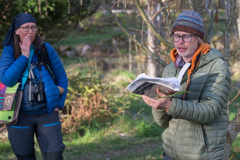 Biologen Tobias läser ur en bok under naturvandringen, med naturguiden Jenny i bakgrunden.